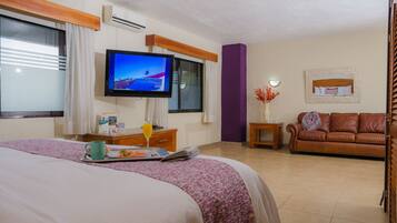 Habitación de hotel con cama, televisor, sofá y una mesita con un jarrón de flores.