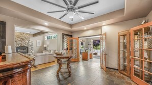 A spacious living area with a stone fireplace, a ceiling fan, and a view into the backyard. - Camano Island Inn (Camano Island)