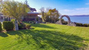 A well-maintained lawn with a stone archway and a house with a covered patio area. - Camano Island Inn (Camano Island)