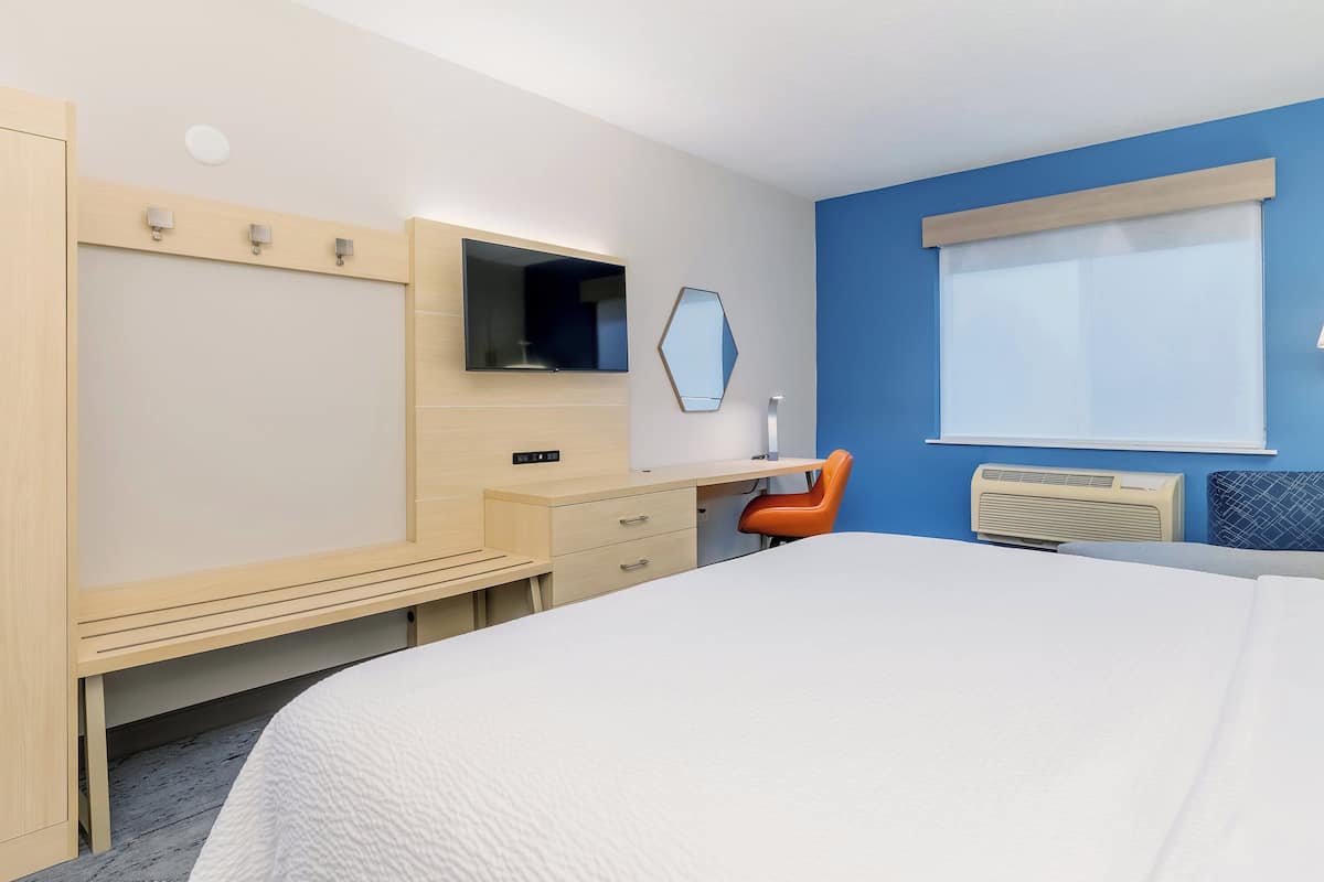 A hotel room with a bed, a desk, a chair, a TV, a mirror, and a window.