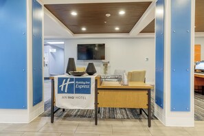 A reception desk with a 'Holiday Inn Express' sign, a flat-screen TV, and a 'Holiday Inn Express' banner. - Holiday Inn Express Hotel & Suites Medford-Central Point by IHG (Central Point)