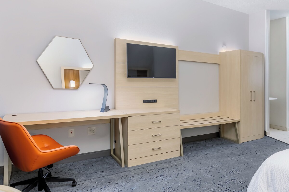 A hotel room with a desk, chair, wardrobe, and a bed.