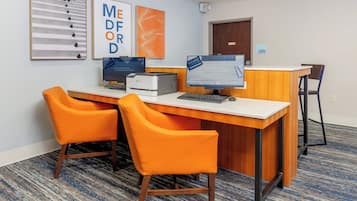 Una recepción con dos sillas naranjas, una computadora e impresora.