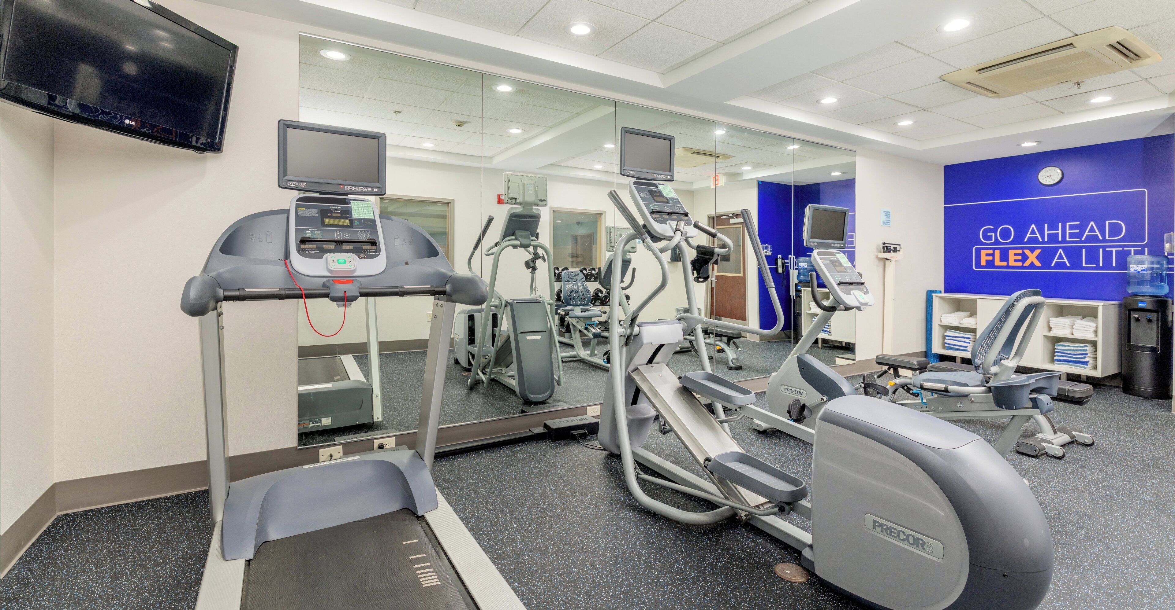 A gym with treadmills, elliptical machines, and a mirrored wall.