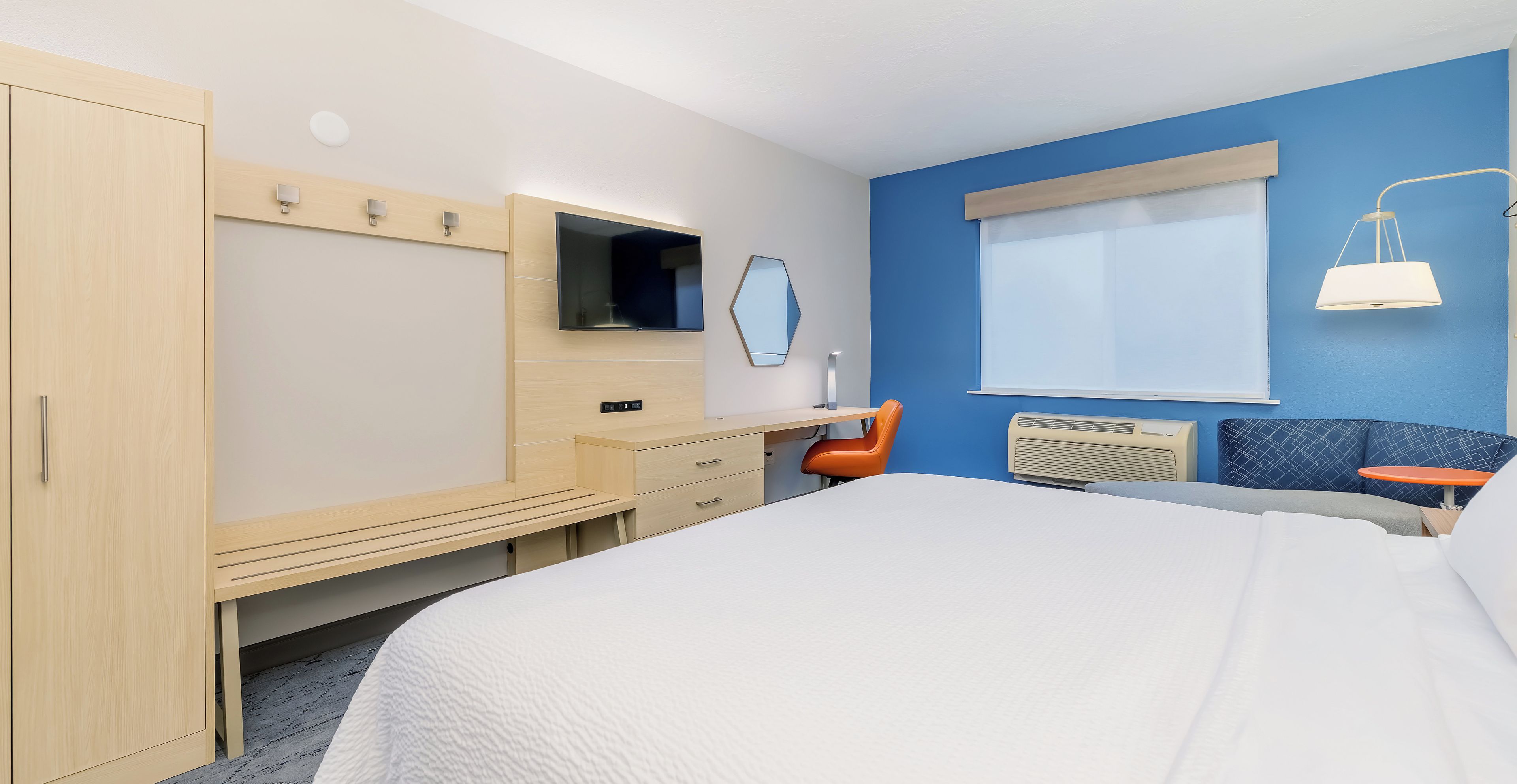 Ein Hotelzimmer mit Bett, Schreibtisch, Stuhl, Fernseher, Spiegel und Fenster.