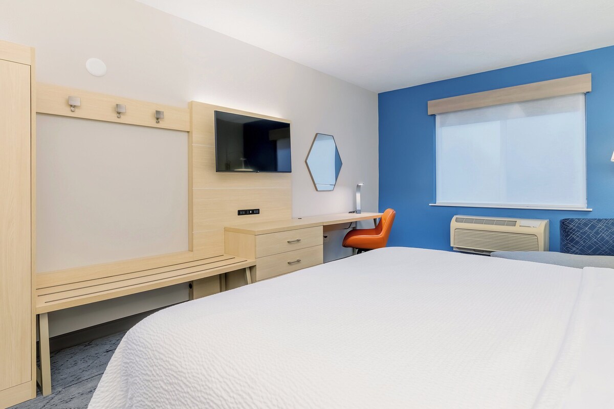 A hotel room with a bed, a desk, a chair, a TV, a mirror, and a window.