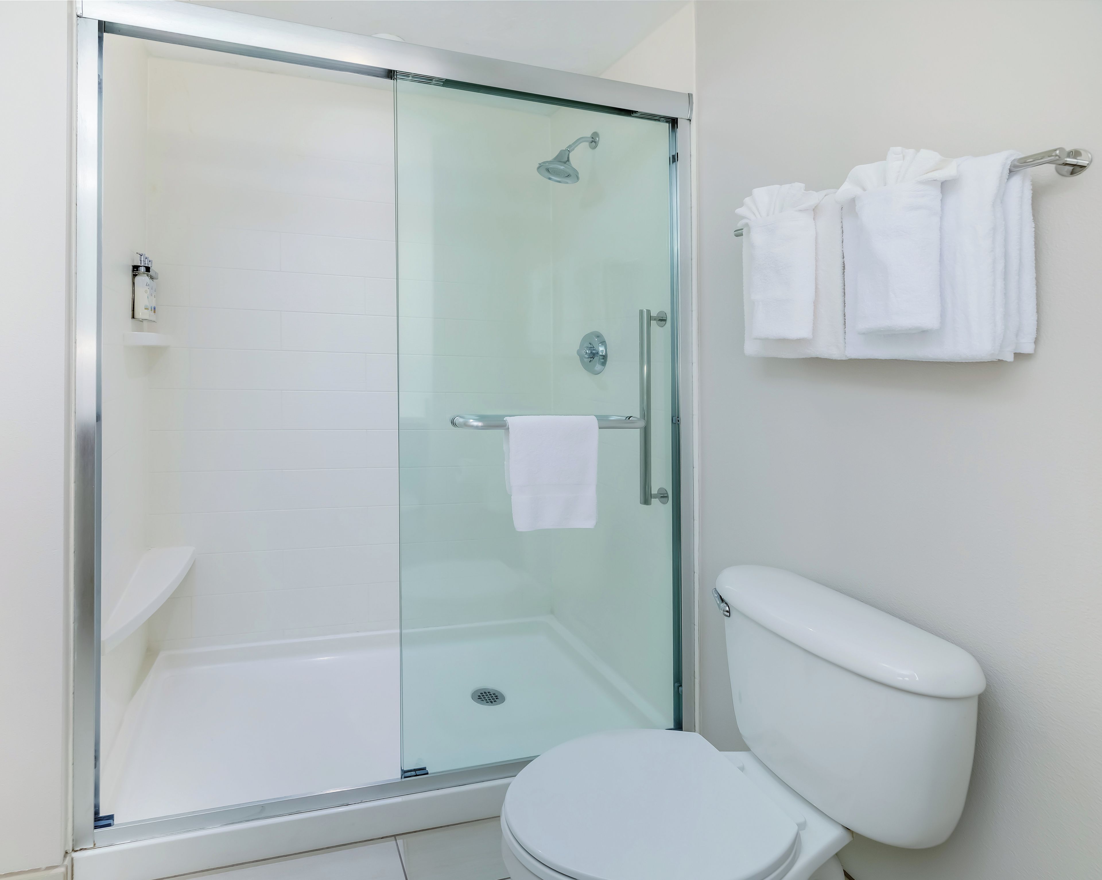 A bathroom with a glass-enclosed shower, a white toilet, and a towel rack with folded towels.