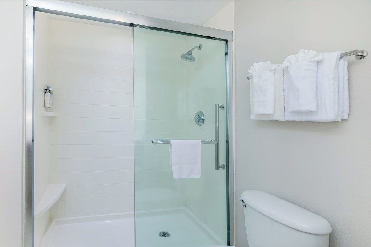 A bathroom with a glass-enclosed shower, a white toilet, and a towel rack with folded towels.