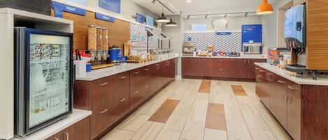 A modern kitchen area with a refrigerator, coffee machine, and various food items on the counter.
