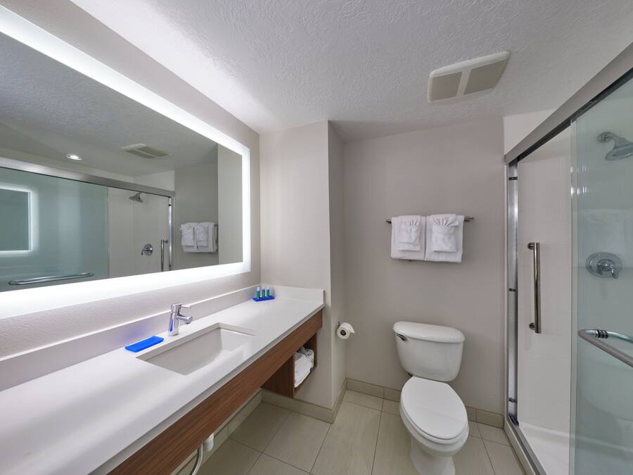 A modern bathroom with a large mirror, a white sink, a toilet, and a glass-enclosed shower.