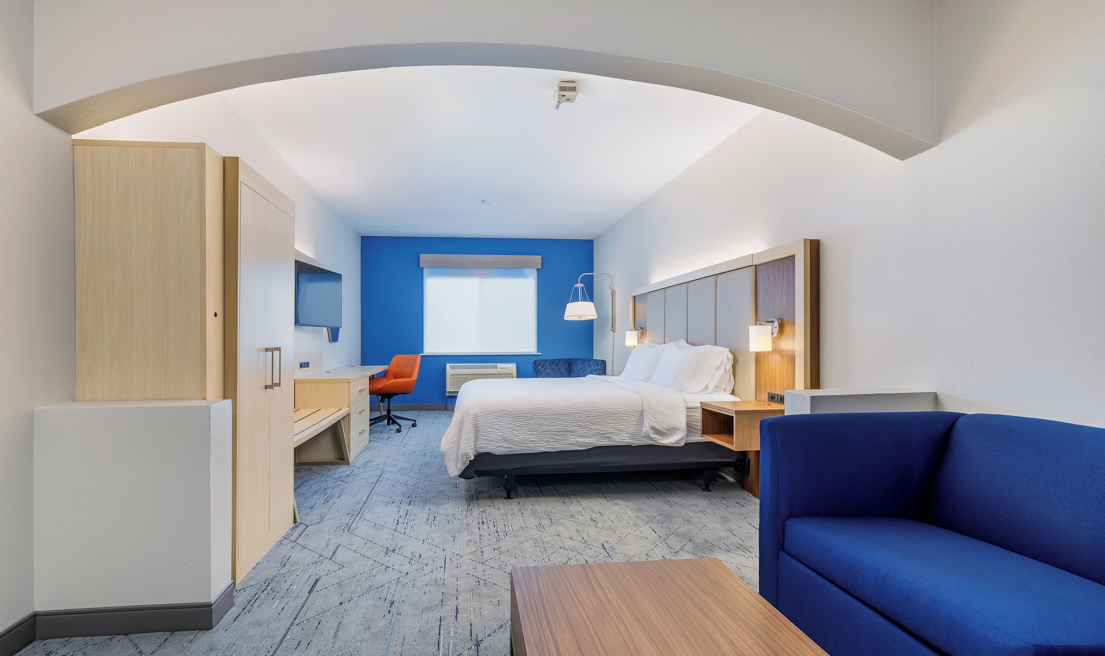 Una habitación de hotel con cama, escritorio, silla, sofá azul y ventana.