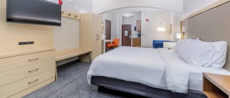 A hotel room with a bed, a desk, a chair, a TV, and a wardrobe.