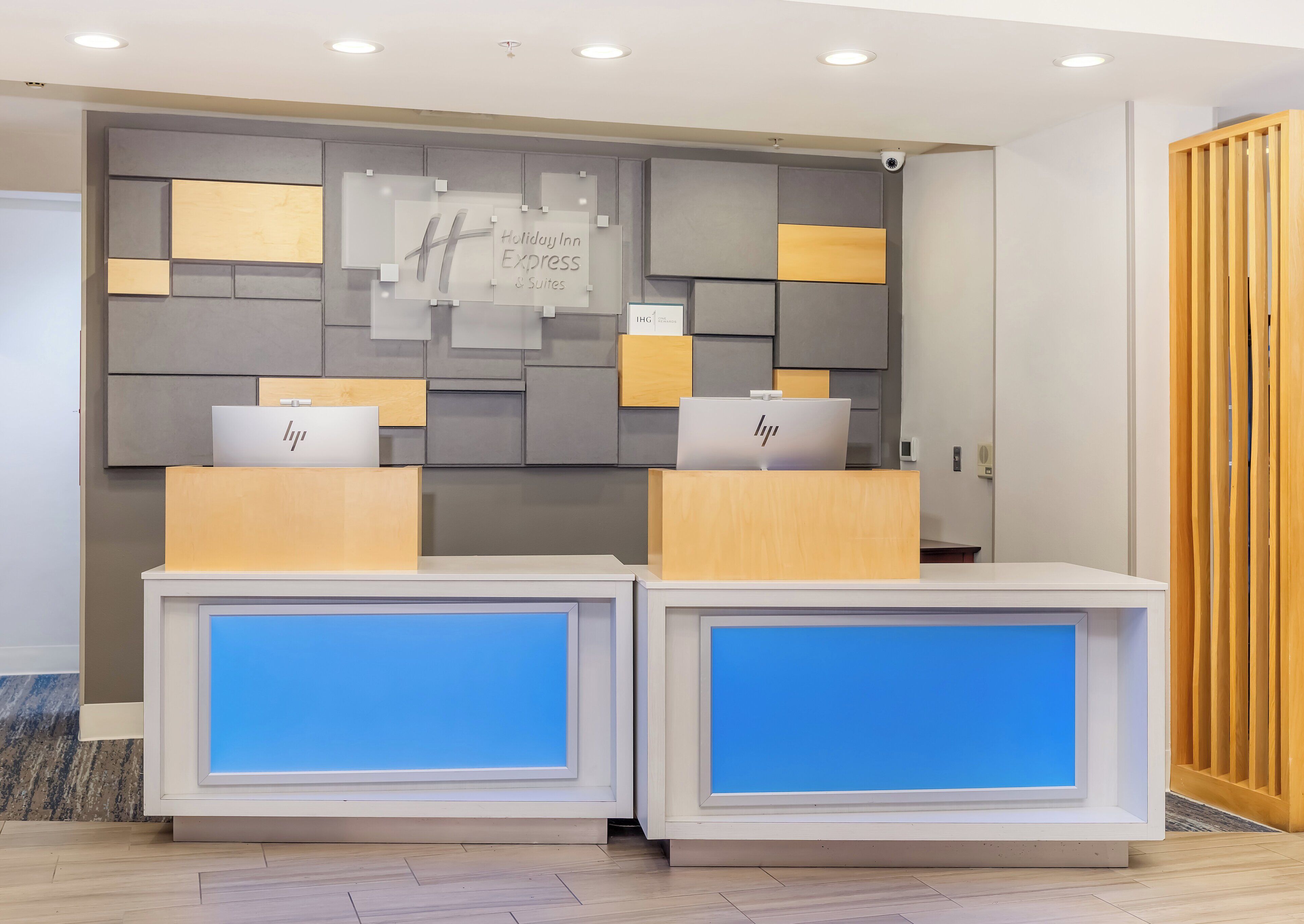 A reception desk with a Holiday Inn Express sign, two HP laptops, and a modern design with grey and wooden panels.