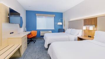 Ein Hotelzimmer mit zwei Betten, einem Schreibtisch, einem orangefarbenen Sessel, einem Fenster mit Jalousien und einem an der Wand befestigten Fernseher.