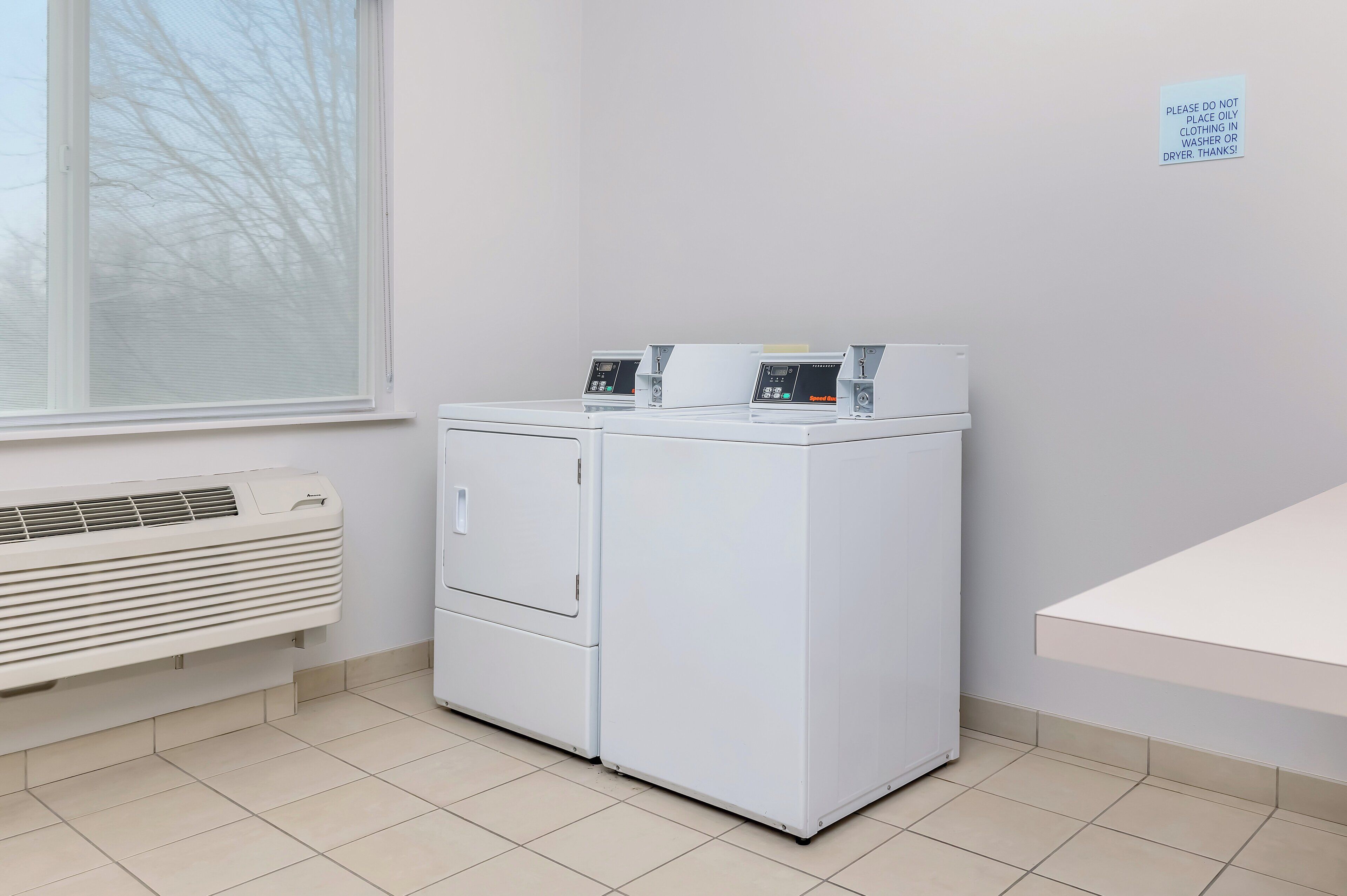 A laundry room with two front-loading washing machines, a vented air conditioner, and a window.