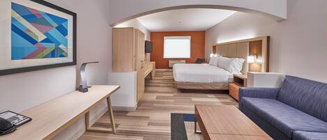 A hotel room with a bed, a desk, a sofa, a TV, and a large abstract painting on the wall.