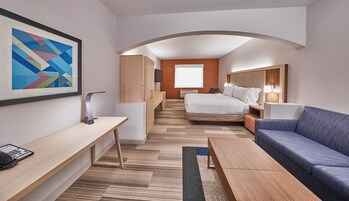 A hotel room with a bed, a desk, a sofa, a TV, and a large abstract painting on the wall.