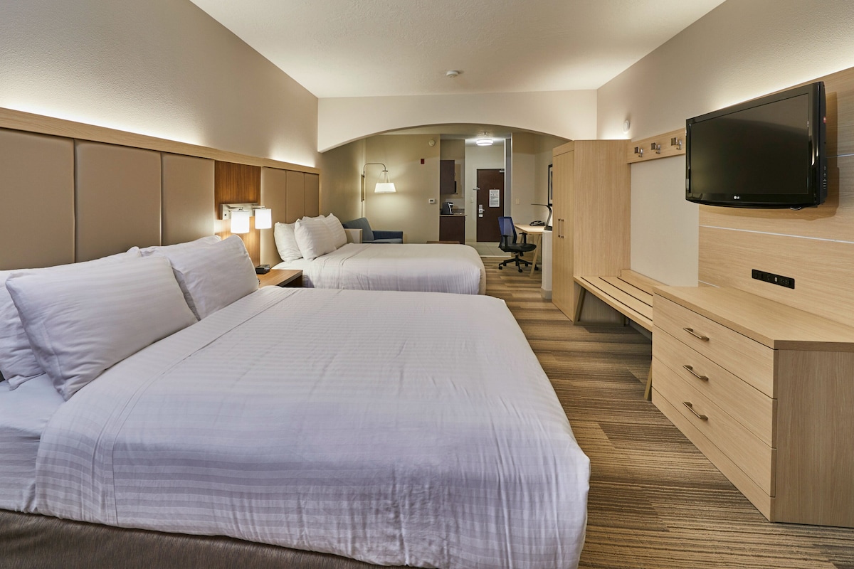 A hotel room with two beds, a desk, a chair, a TV, and a wardrobe.