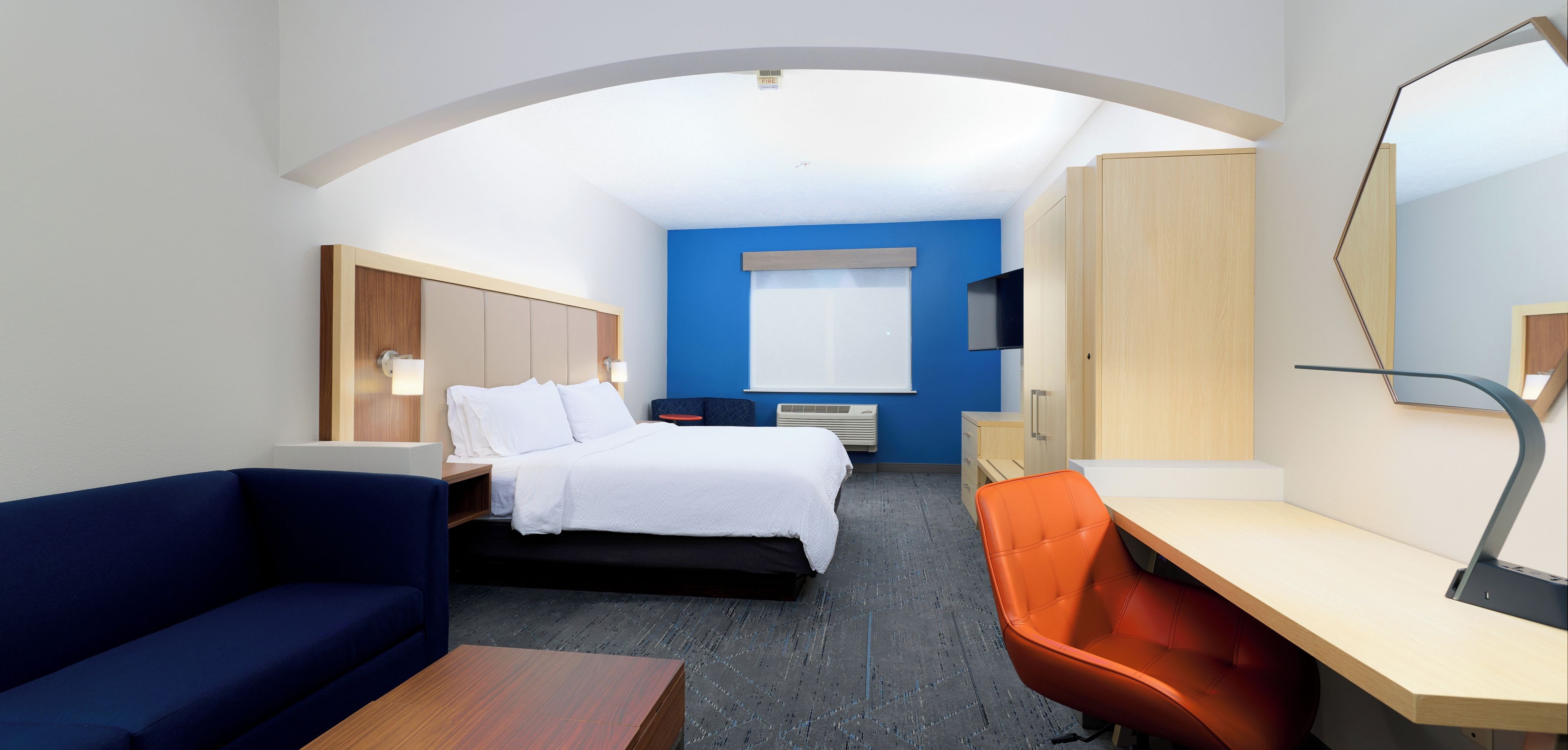 A hotel room with a bed, a desk, a chair, a sofa, and a television.