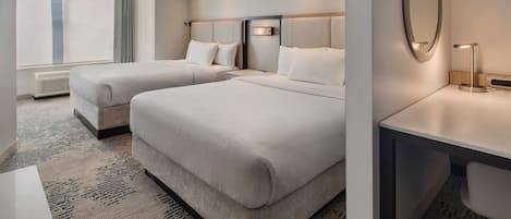 A hotel room with two beds, a desk, a mirror, and a large window.