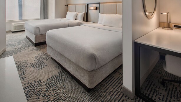 Une chambre d’hôtel avec deux lits, un bureau, un miroir et une grande fenêtre.