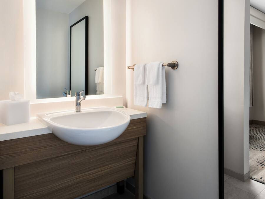 Un baño moderno con un lavamanos grande de color blanco, tocador de madera, un espejo y un perchero para toallas.