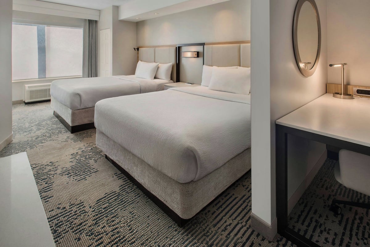 Habitación de hotel con dos camas, un escritorio, un espejo y un ventanal grande.