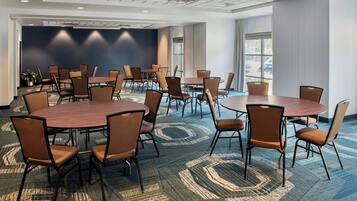 A conference room with multiple tables and chairs, carpeted flooring, and a large window providing natural light.
