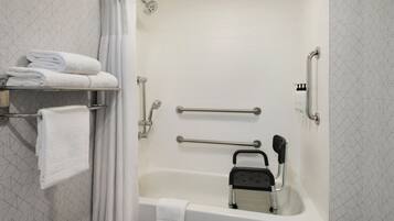 Un baño moderno con bañera, barras de apoyo, asiento de ducha y toallas ordenadas en un estante.
