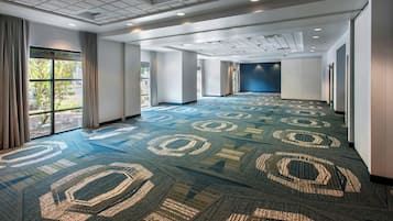 A spacious hotel corridor with patterned carpet, large windows, and a modern ceiling design.