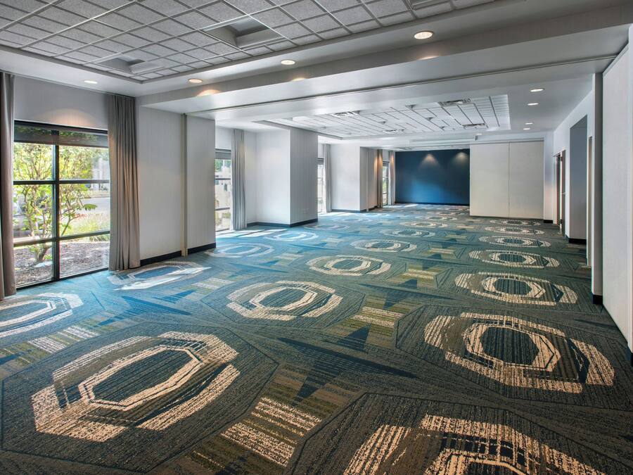A spacious hotel corridor with patterned carpet, large windows, and a modern ceiling design.