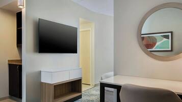 Ett modernt hotellrum med en platt-TV, en rund spegel, ett litet vitt bord och ett inbyggt träskåp.