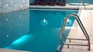 A modern indoor swimming pool with a clear water surface, a metal ladder, and a seating area with chairs. - Hotel de Guimarães (Guimarães)