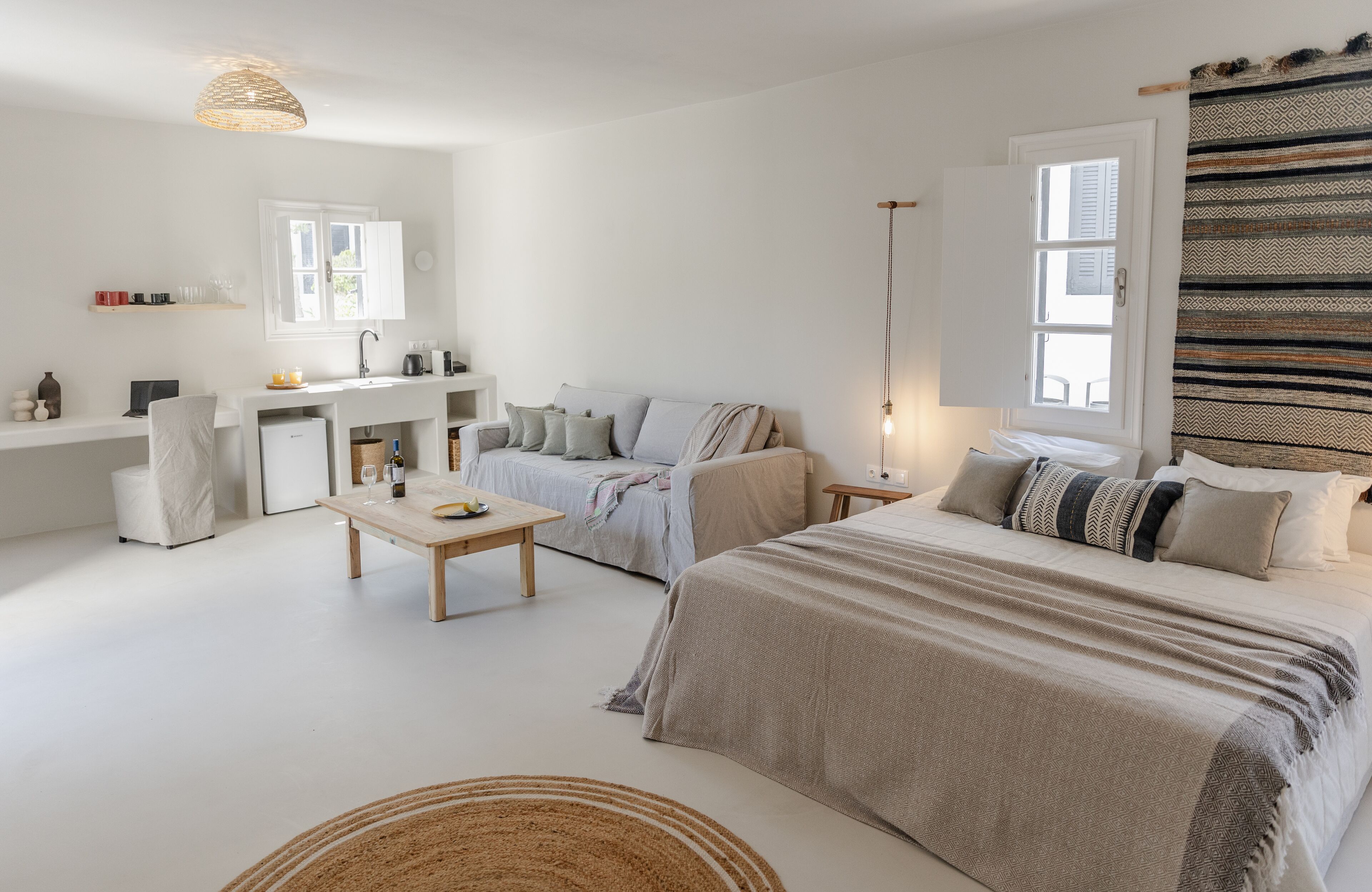 Une chambre à coucher moderne et minimaliste, dotée d’un grand lit, d’un petit canapé, d’une table à manger et d’un coin cuisine.