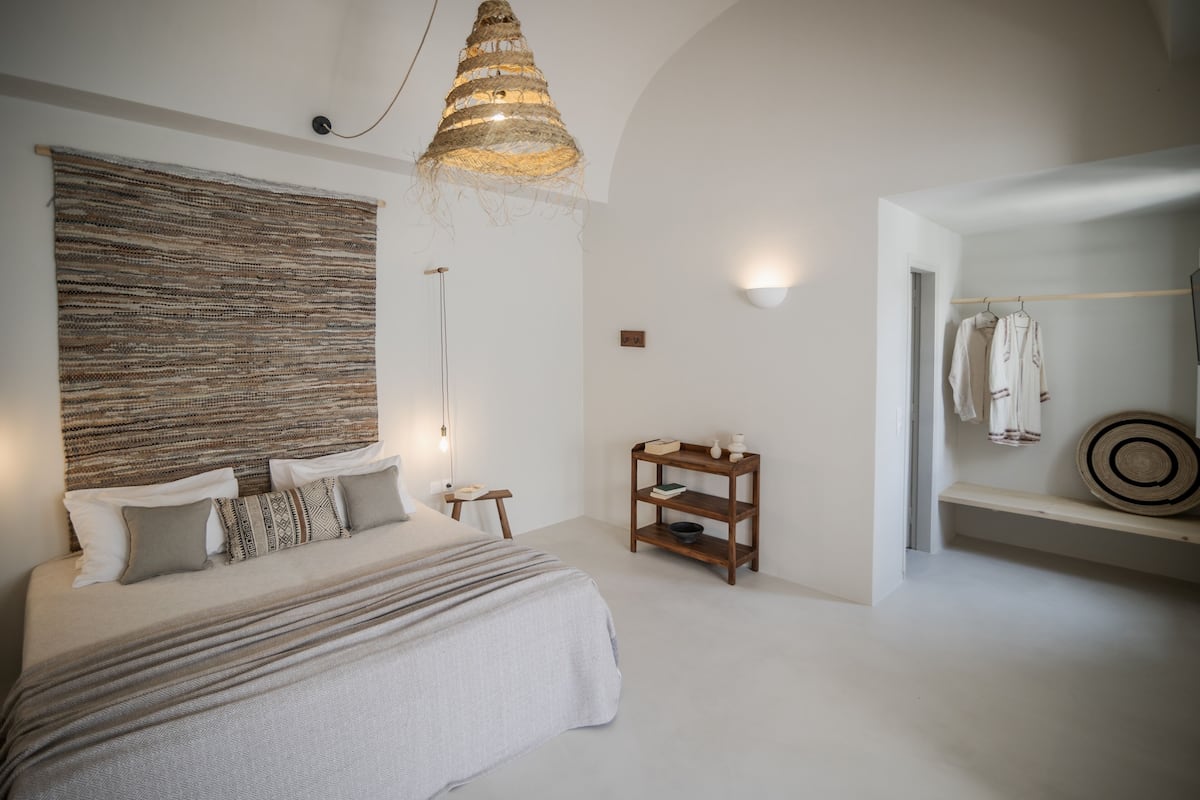 Un dormitorio con una cama grande, una lámpara colgante, una mesita de noche de madera y un estante con un espejo y una toalla.