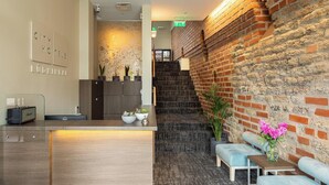 A reception area with a wooden reception desk, a brick wall, and a staircase leading to an upper floor. - City Hotels Rūdninkai (Vilnius)