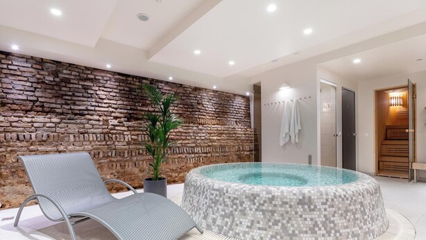 A modern bathroom with a stone wall, a glass-enclosed hot tub, and a metal chair. - City Hotels Rūdninkai (Vilnius)