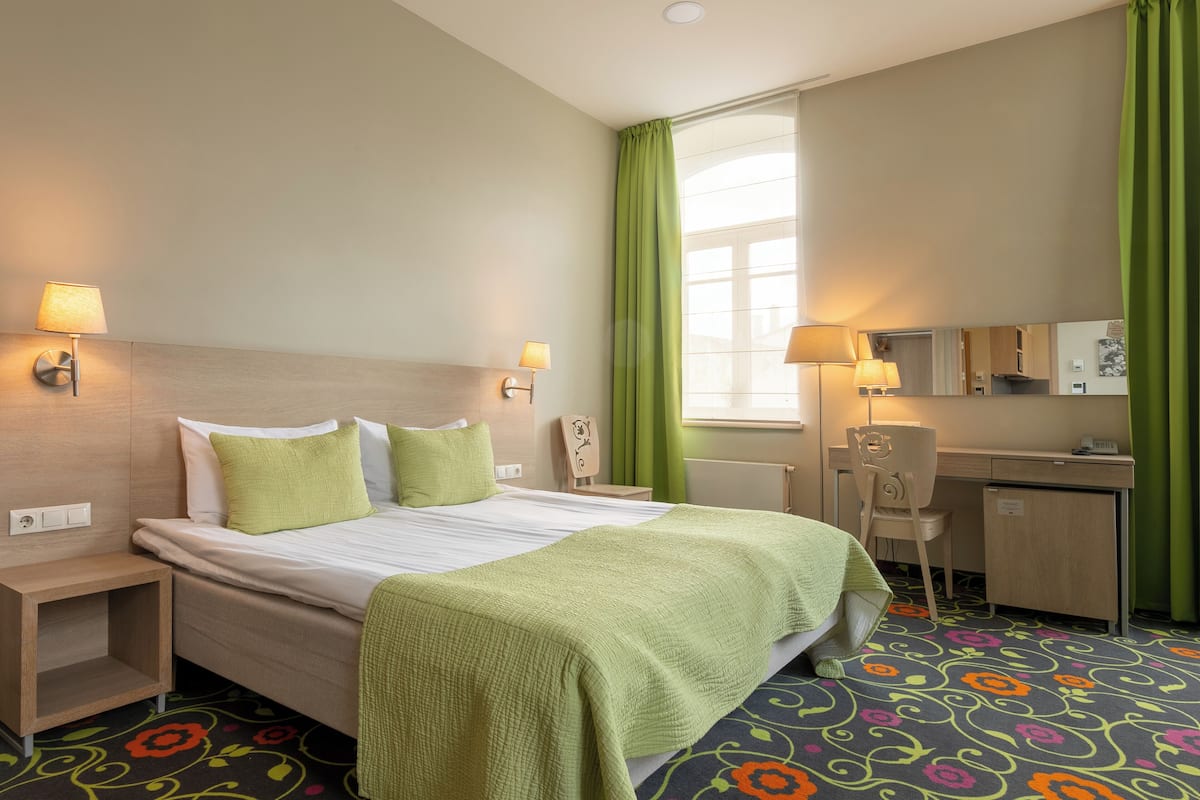 A hotel room with a bed, bedside tables, a desk, and a chair.