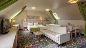 A hotel room with a bed, a sofa, a desk, a TV, and a window with curtains. - City Hotels Rūdninkai (Vilnius)