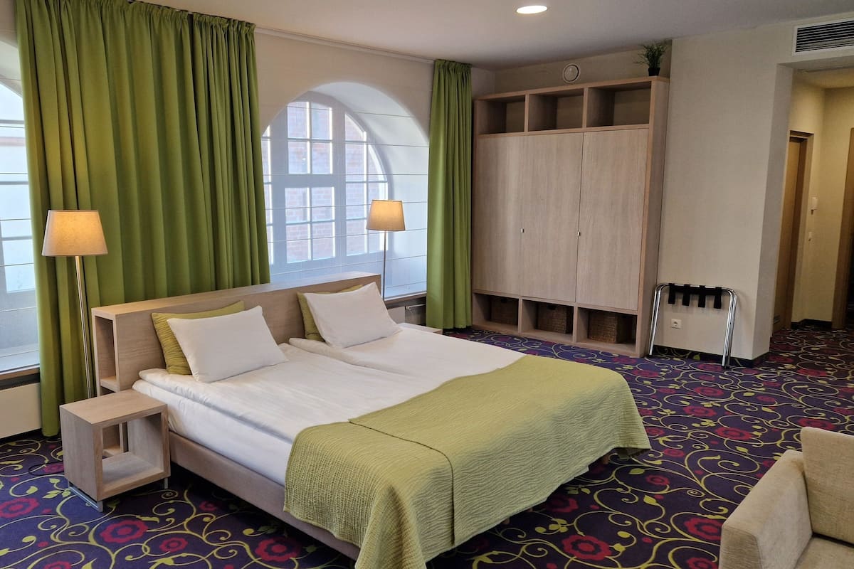 A hotel room with a large bed, two bedside lamps, a wardrobe, and a patterned carpet.
