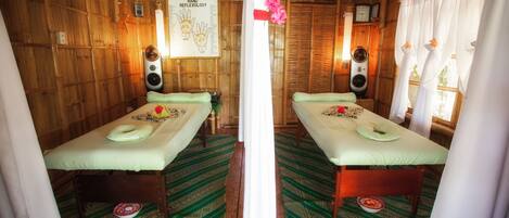 A room with two massage tables, wooden walls, a hand reflexology chart, and a clock.