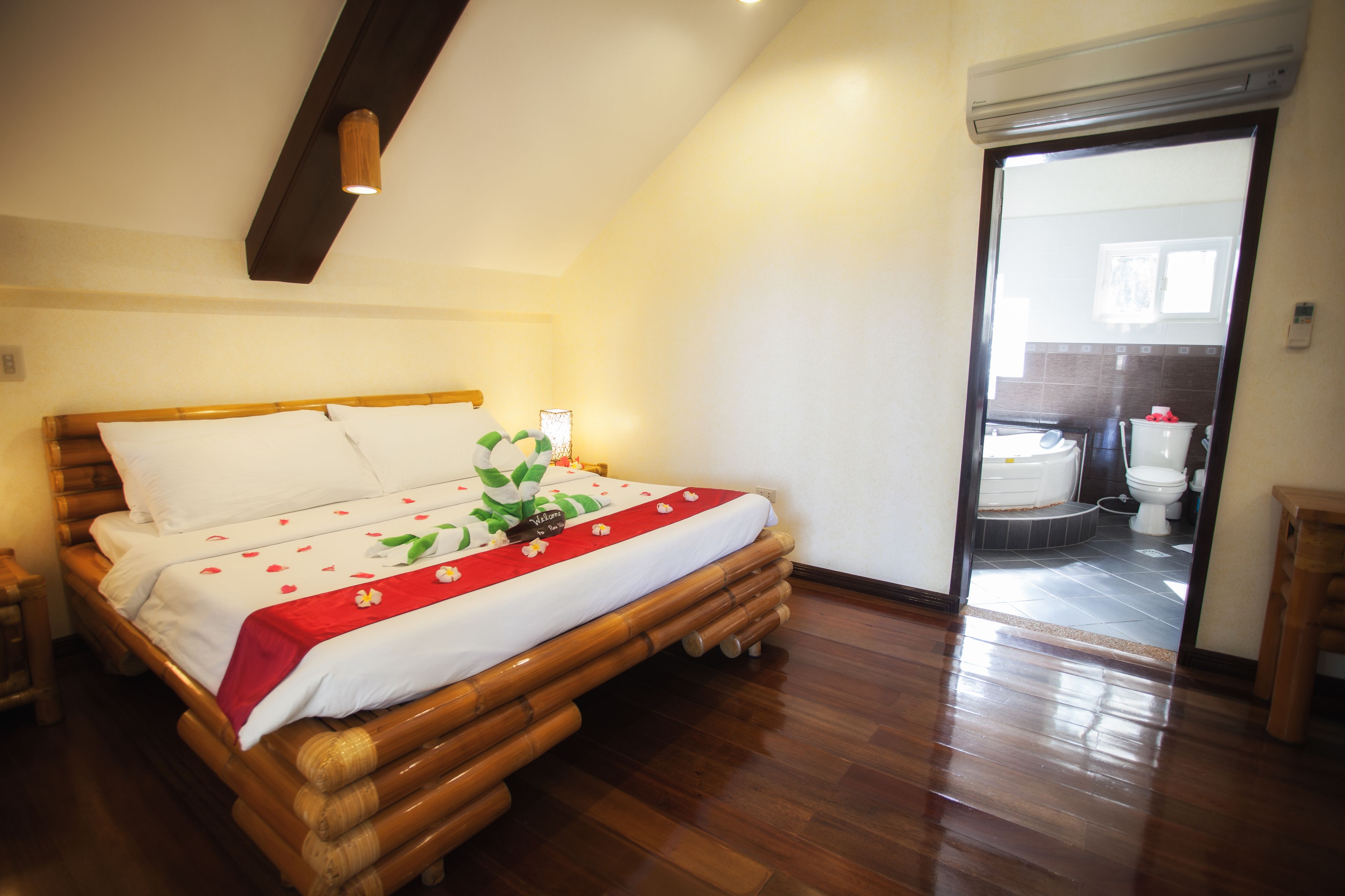 A room with a wooden bed, a small bedside table, and a view of the bathroom through an open door.