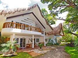 A two-story building with a thatched roof, a balcony with wooden railings, and a garden with various plants.