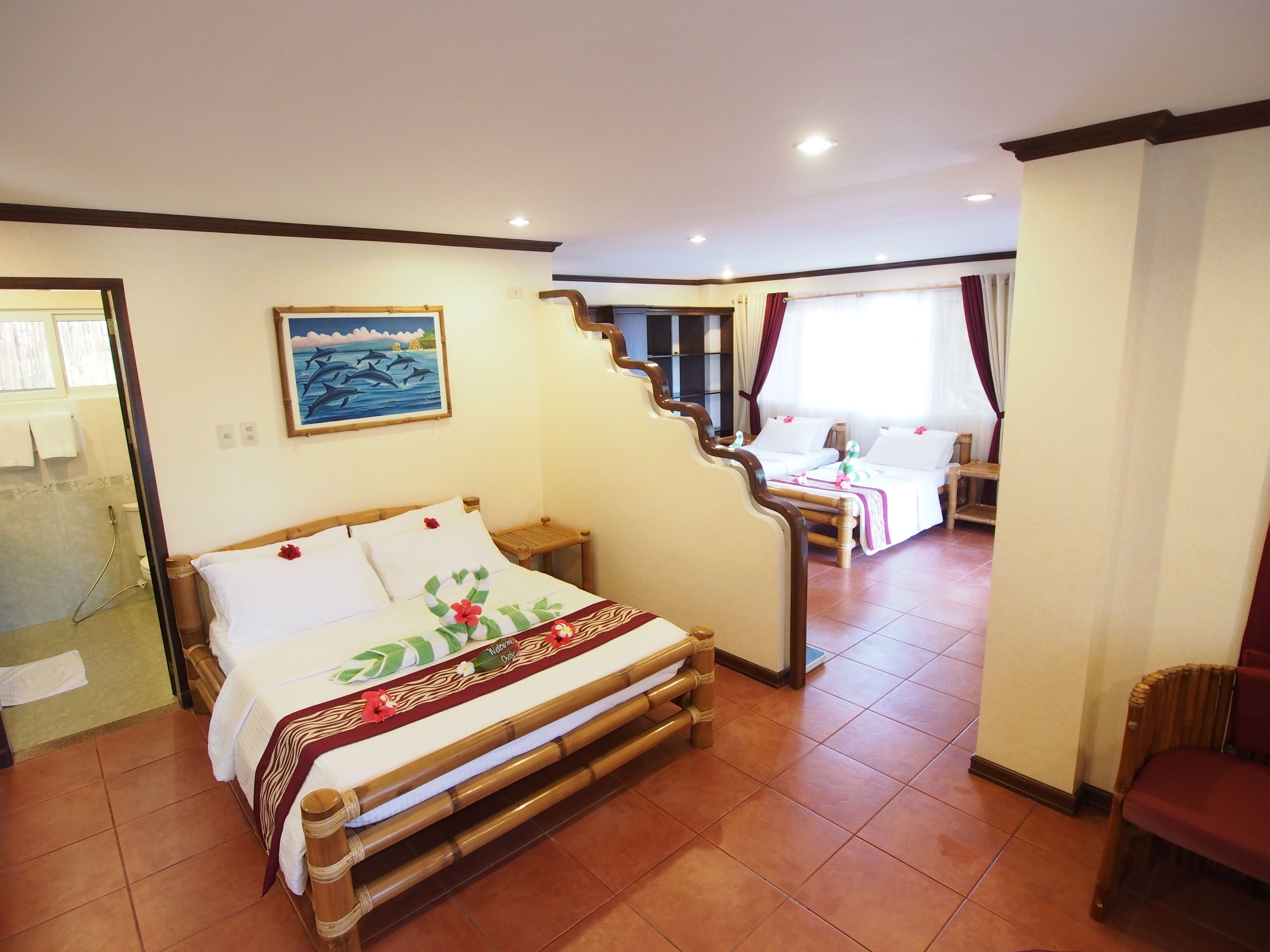 Une chambre d’hôtel avec un lit, une petite table, une chaise, un tableau au mur et une salle de bain visible à travers une porte ouverte.
