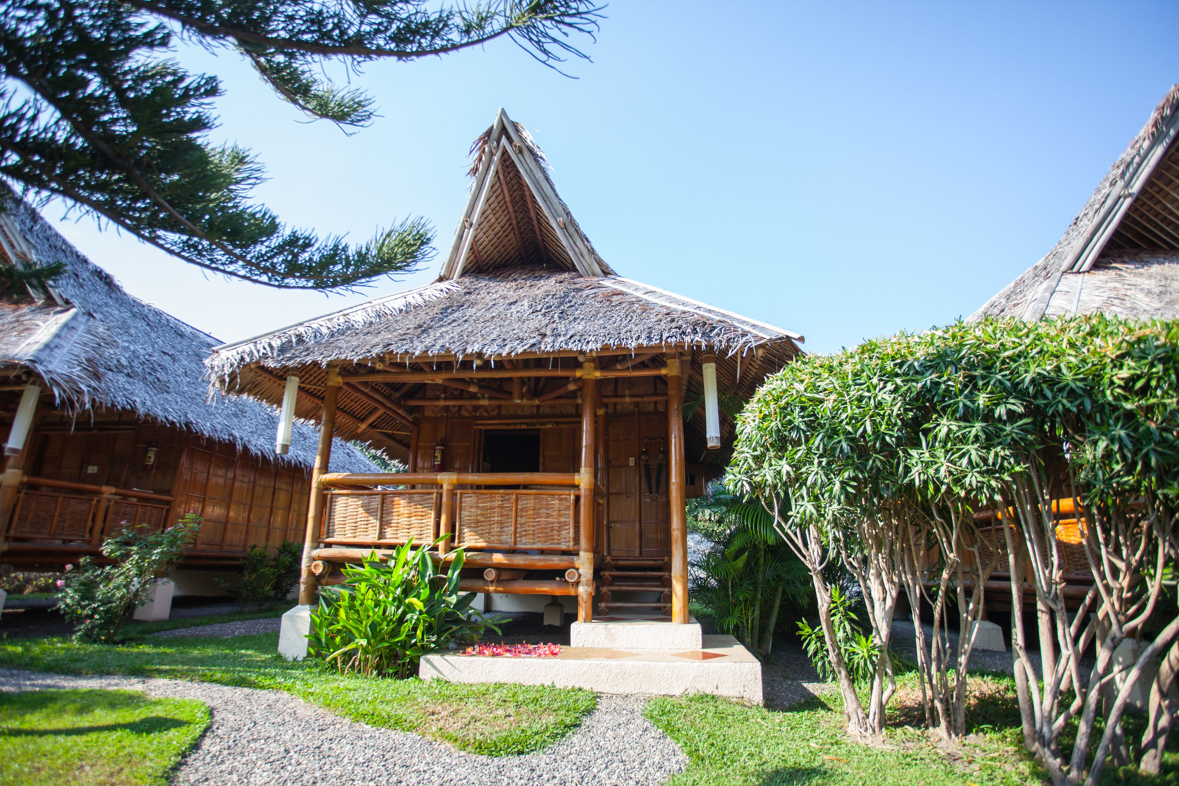 A traditional wooden house with a thatched roof, surrounded by a well-maintained garden with a gravel path.