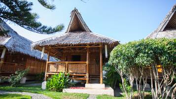 A traditional wooden house with a thatched roof, surrounded by a well-maintained garden with a gravel path.