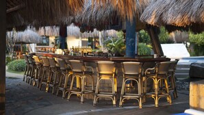 Een terras met een bar, rieten stoelen en een rieten dak.