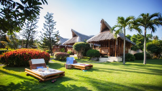 Een resort met rieten bungalows, een verzorgd gazon en tropische beplanting.
