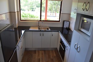 Una cocina compacta con armarios blancos, un lavamanos de acero inoxidable y un microondas.