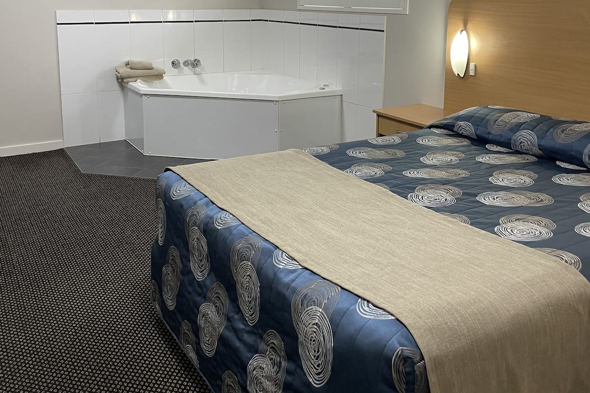 Une chambre d’hôtel avec un grand lit, une baignoire, une fenêtre avec des stores et un luminaire au plafond.